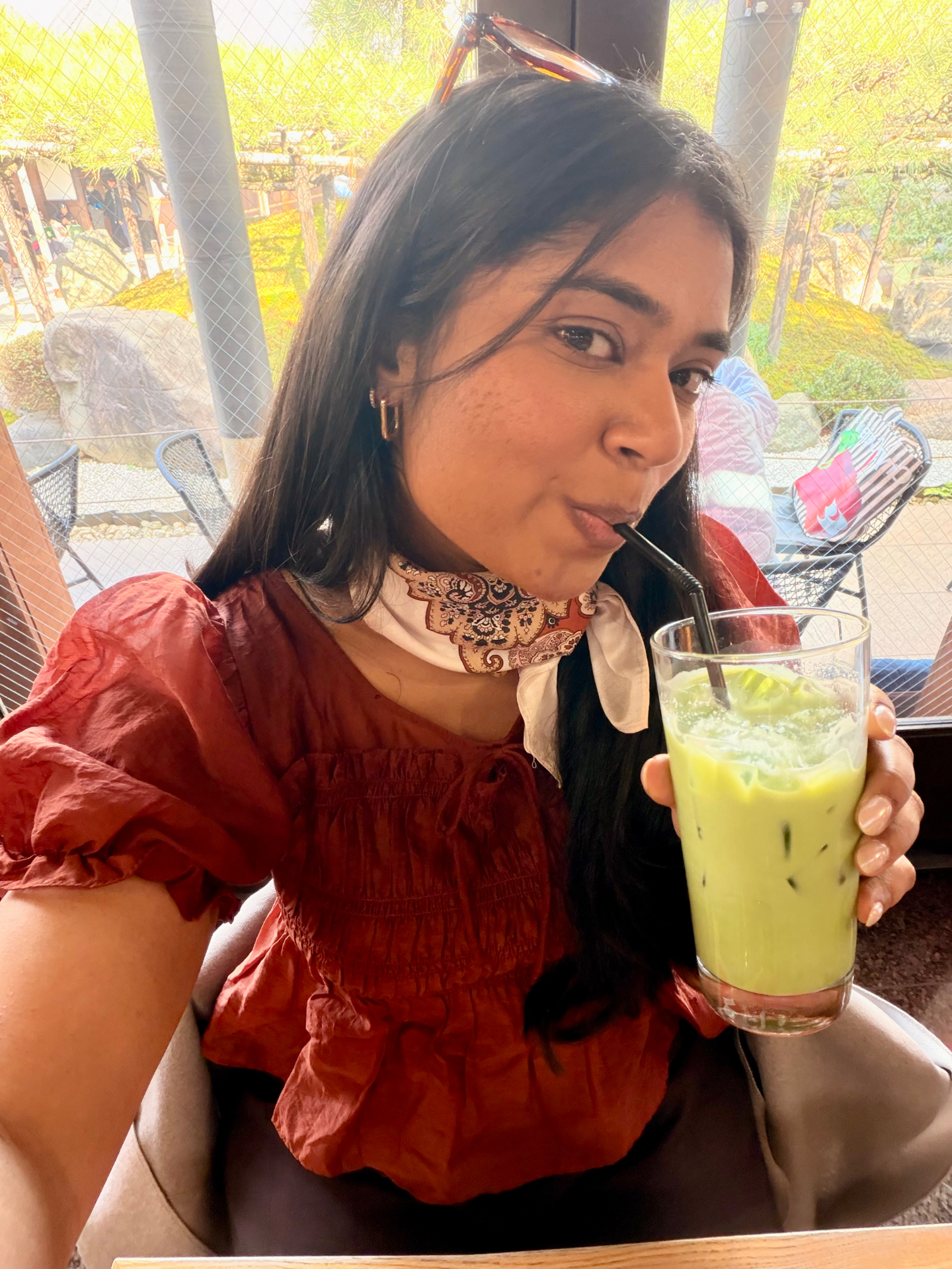 Shruthi sipping an iced matcha latte at a cafe overlooking a Japanese garden